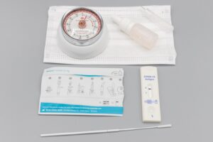 COVID-19 rapid antigen home test kit with test cassette, nasal swab, buffer vial and instruction leaflet on a gray surface