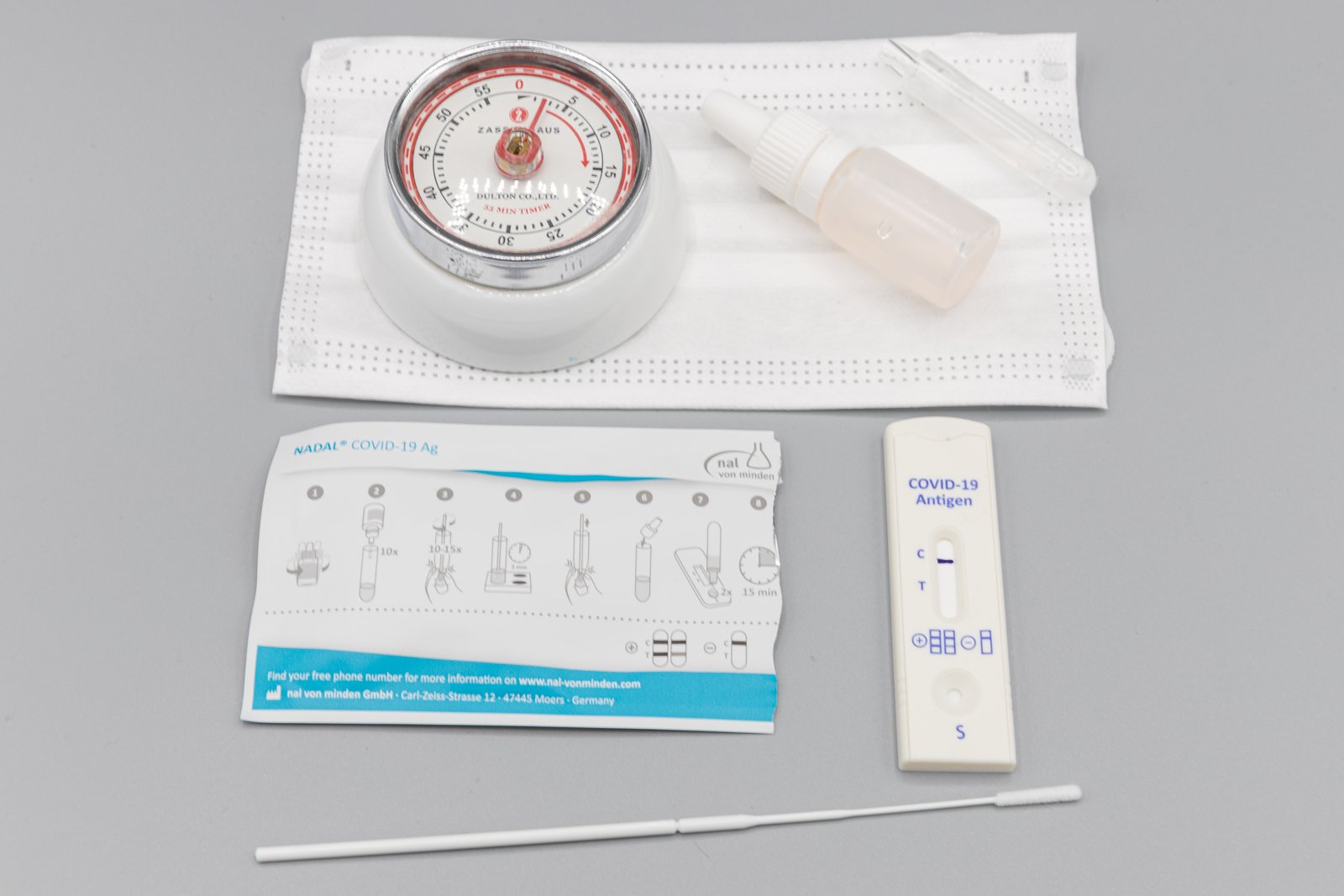 COVID-19 rapid antigen home test kit with test cassette, nasal swab, buffer vial and instruction leaflet on a gray surface